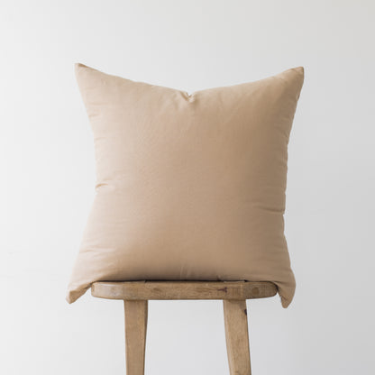 Beige linen pillow cover with envelope closure displayed on wooden stool.