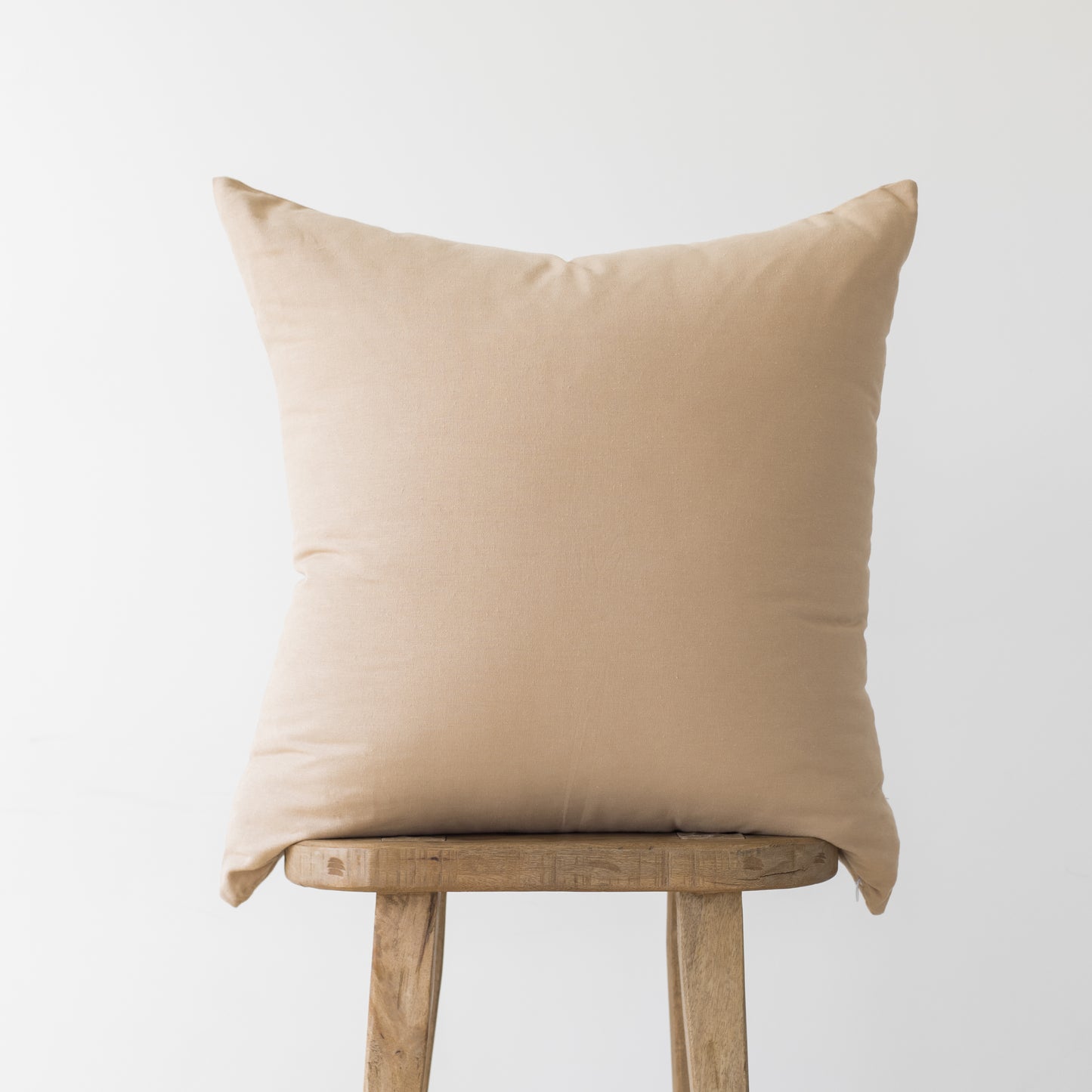 Beige linen pillow cover displayed on wooden chair back against neutral background.