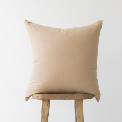 Beige linen pillow cover displayed on wooden chair back against neutral background.