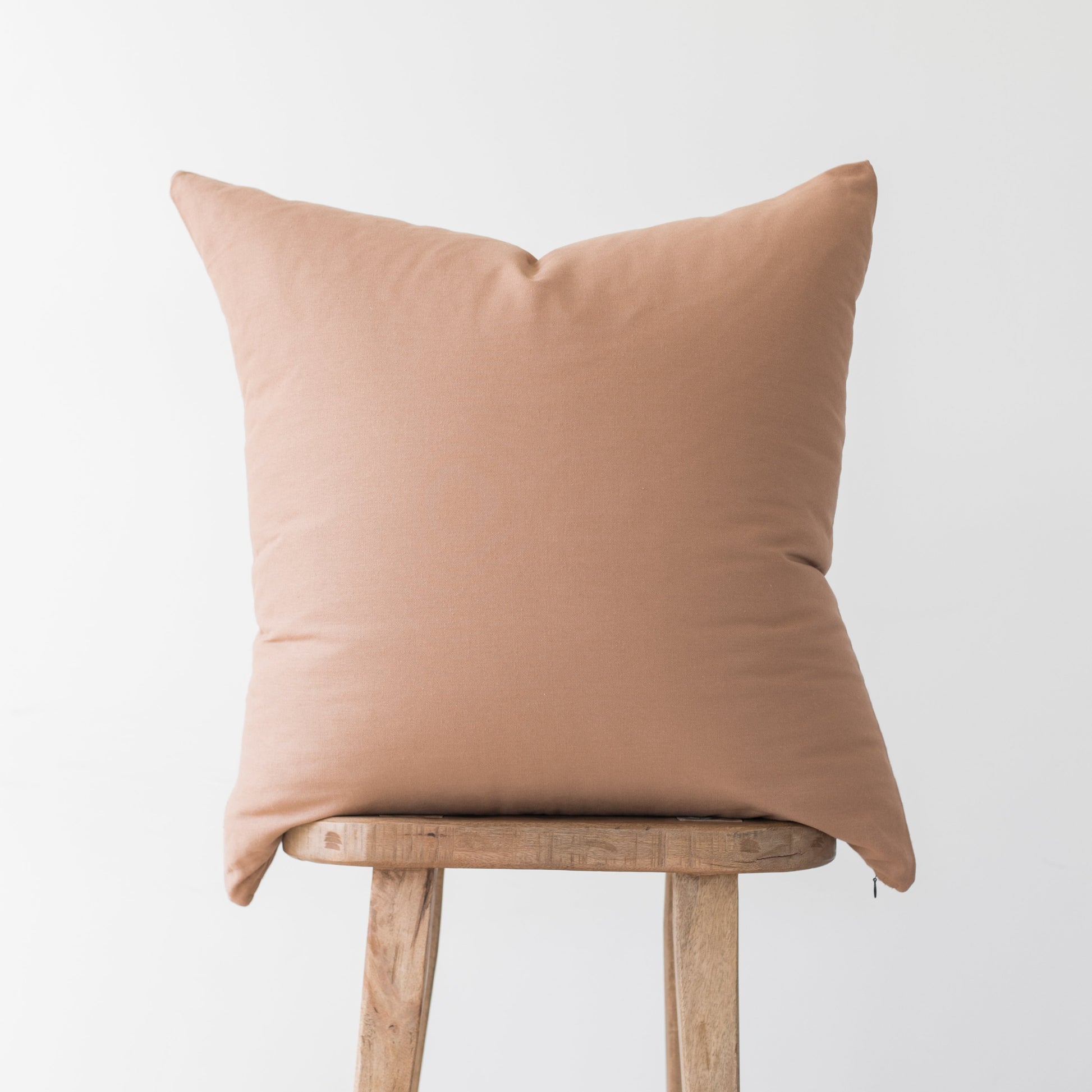 Dusty rose throw pillow with solid fabric displayed on wooden stool.