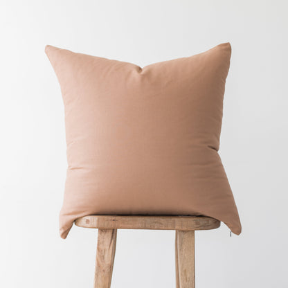 Dusty rose throw pillow with solid fabric displayed on wooden stool.