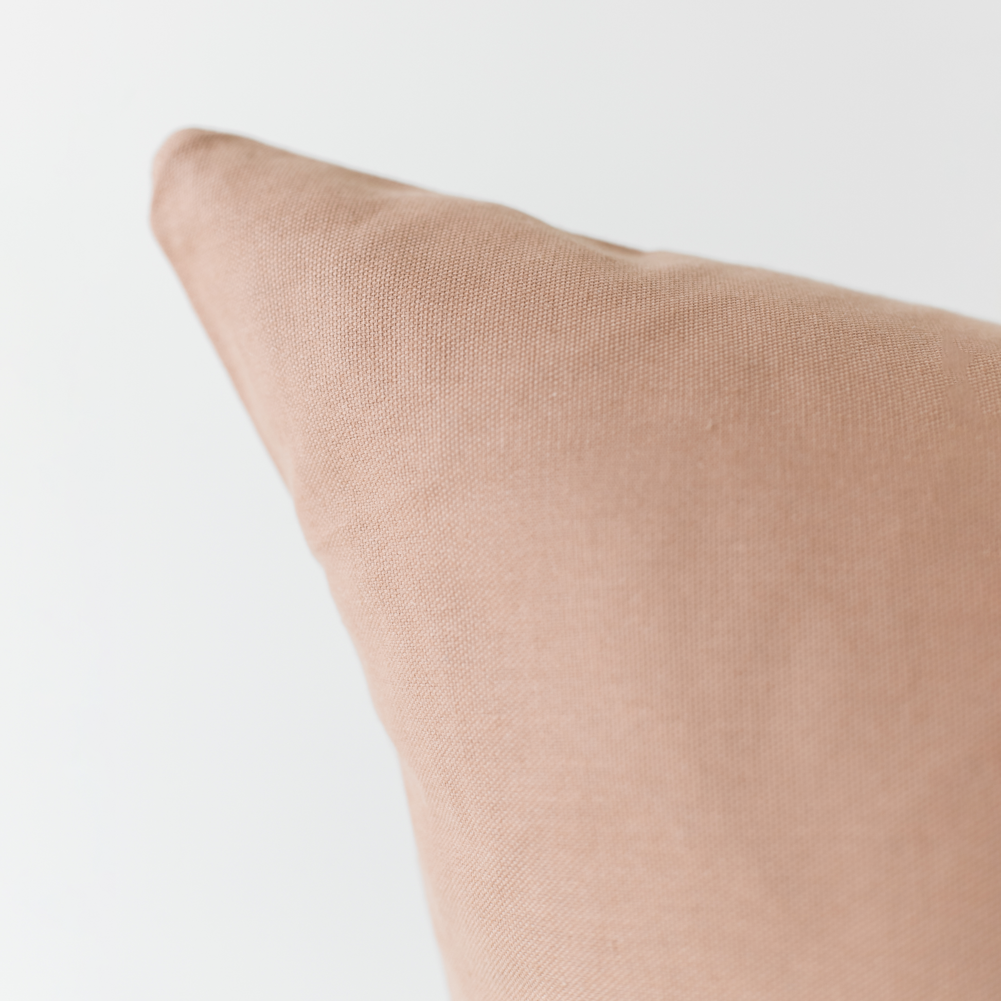 Dusty rose solid-colored pillow with textured fabric surface and angled corner detail.