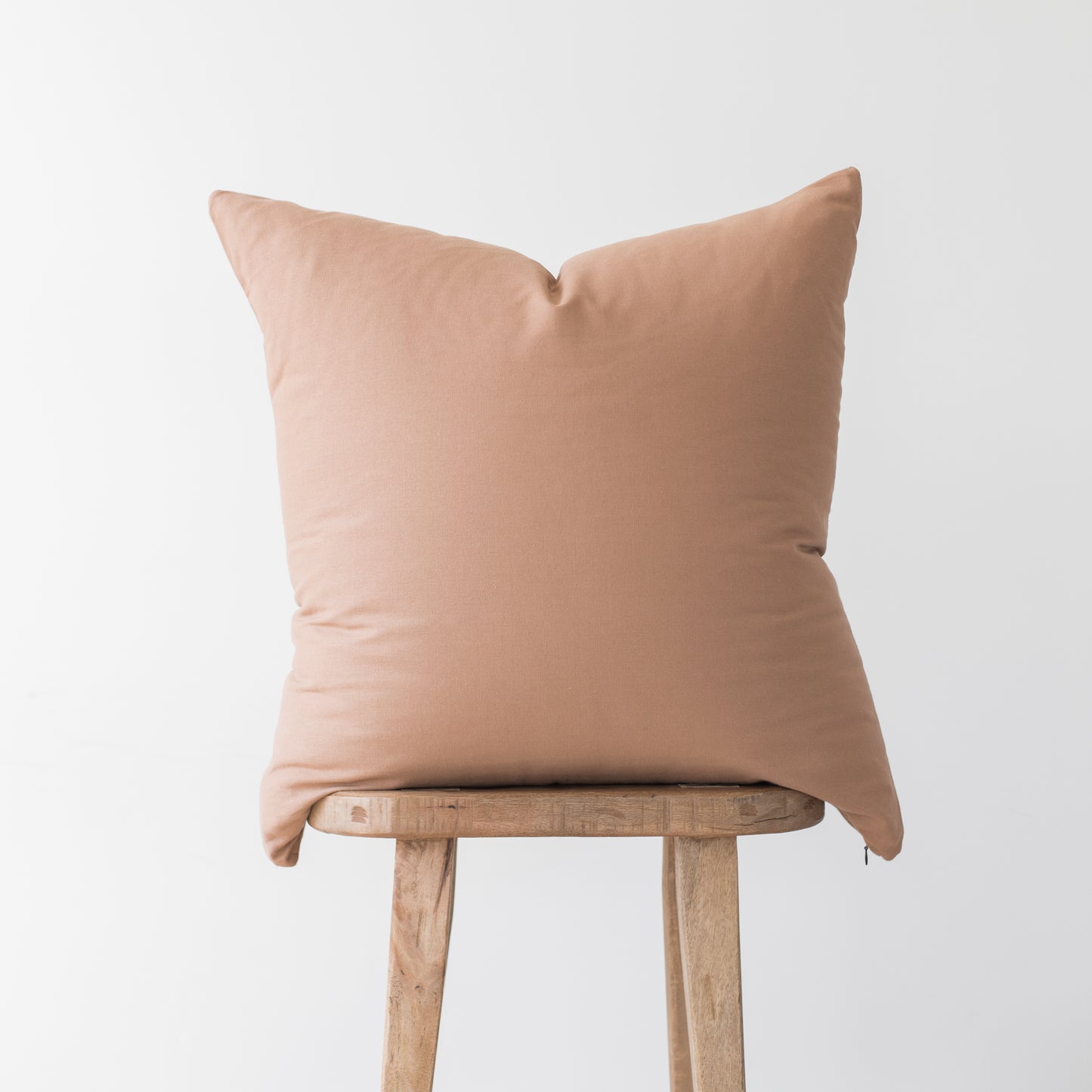 Dusty rose solid throw pillow with envelope closure displayed on wooden stool.