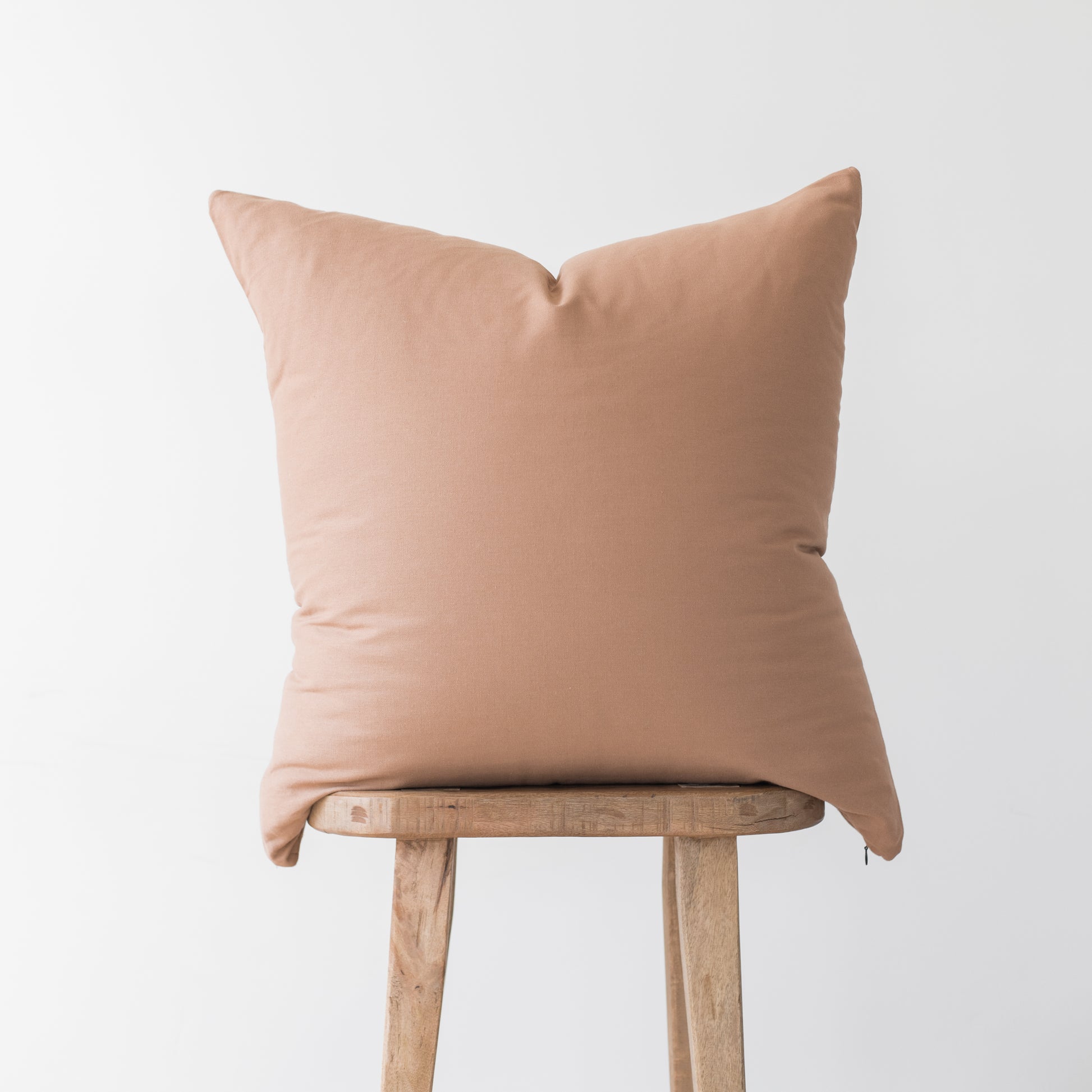 Dusty rose solid throw pillow with envelope closure displayed on wooden stool.