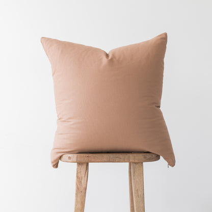 Dusty rose solid throw pillow with envelope closure displayed on wooden stool.