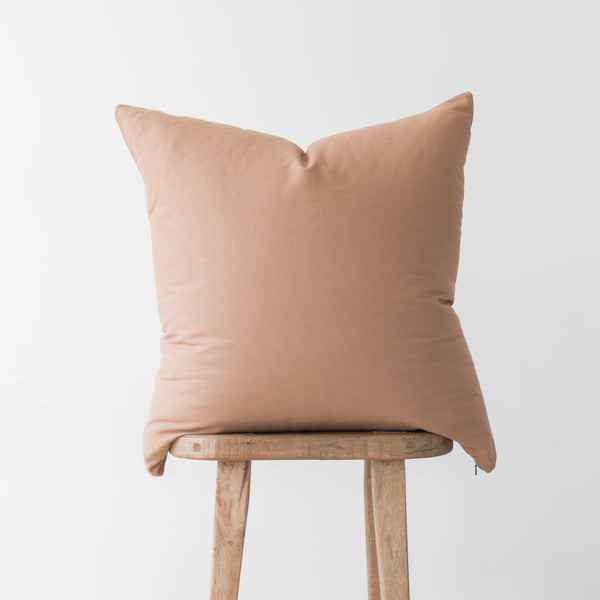 Dusty rose solid throw pillow with envelope closure displayed on wooden stool.