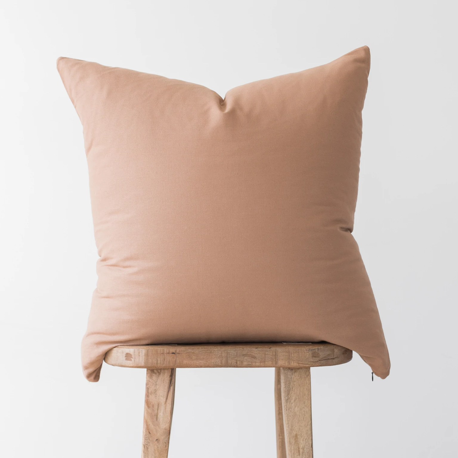 Dusty rose pillow cover with solid color and envelope closure, displayed on wooden stool.