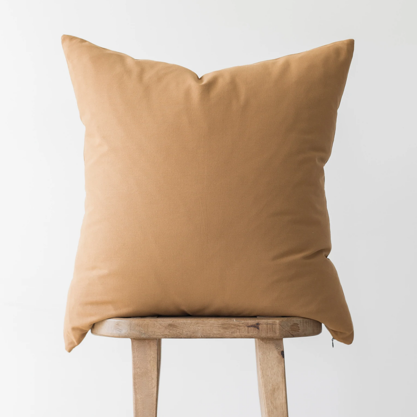 Terracotta-colored square pillow with knife edges displayed on a wooden stool.