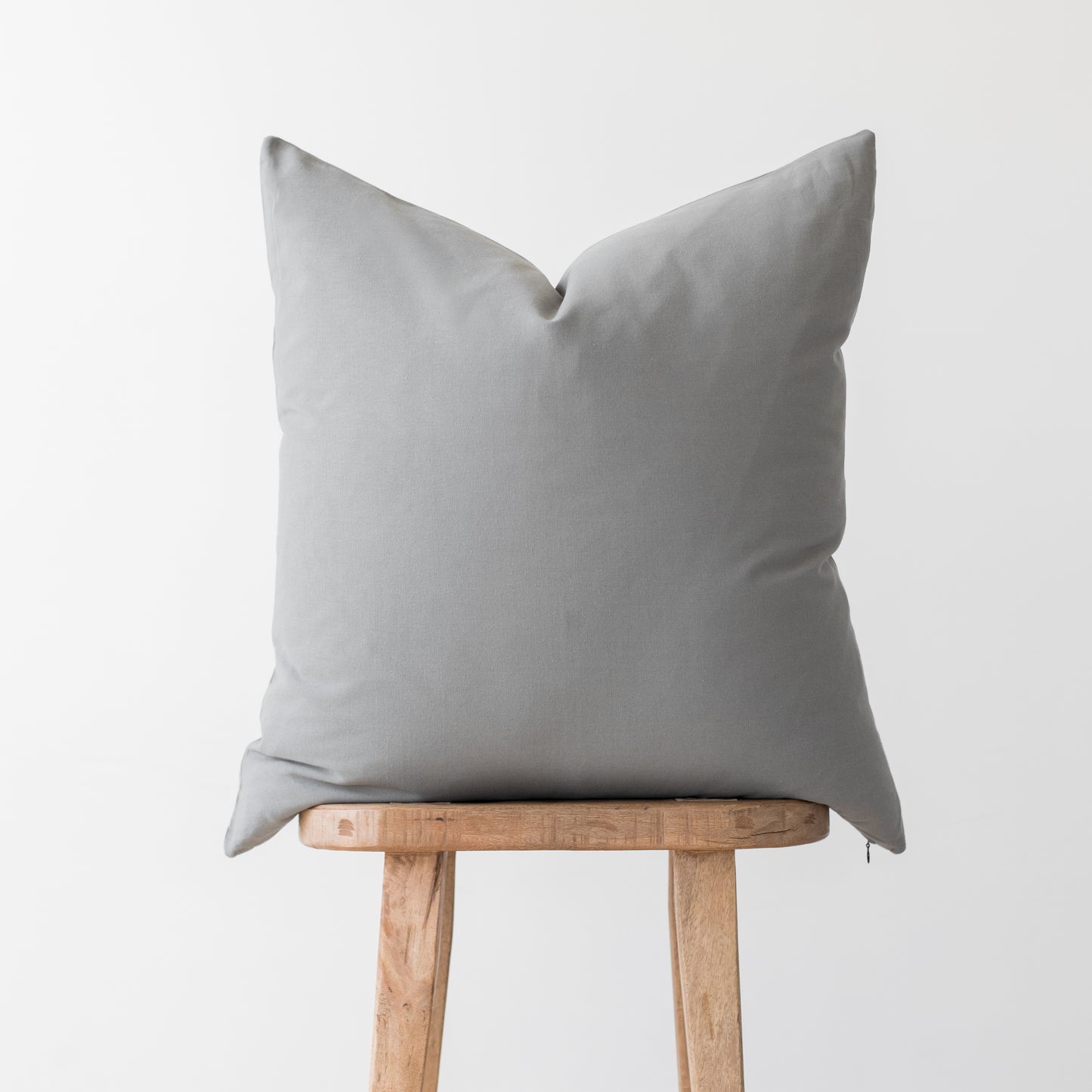 Light gray linen pillow cover with envelope closure displayed on wooden stool.