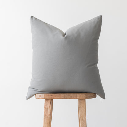Light gray linen pillow cover with envelope closure displayed on wooden stool.