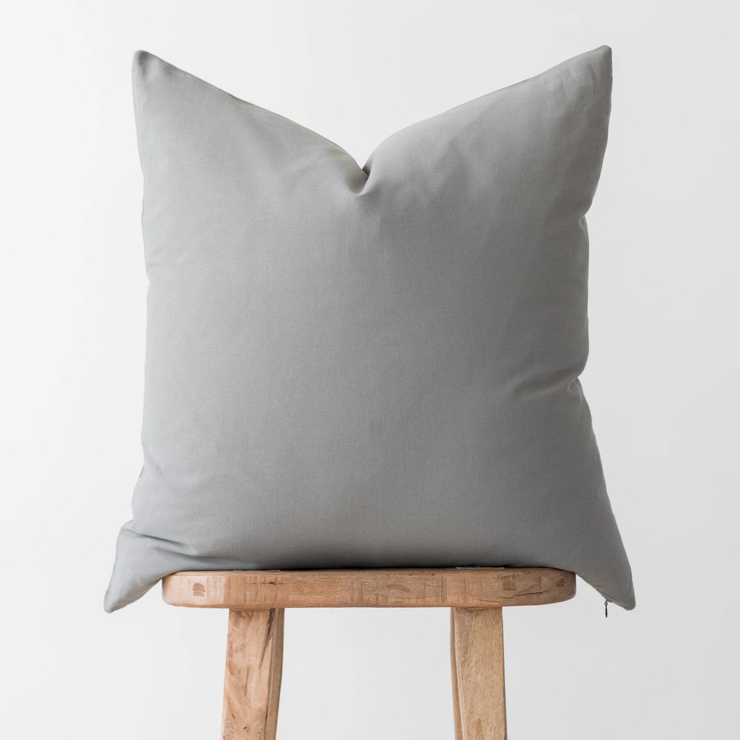 Light gray pillow cover with envelope closure displayed on wooden stool.