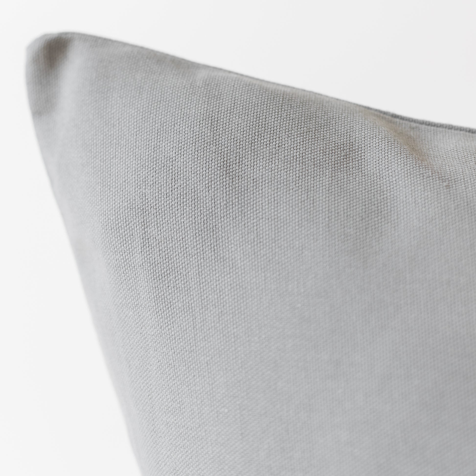 Light gray woven pillow with textured fabric surface and folded corner detail.