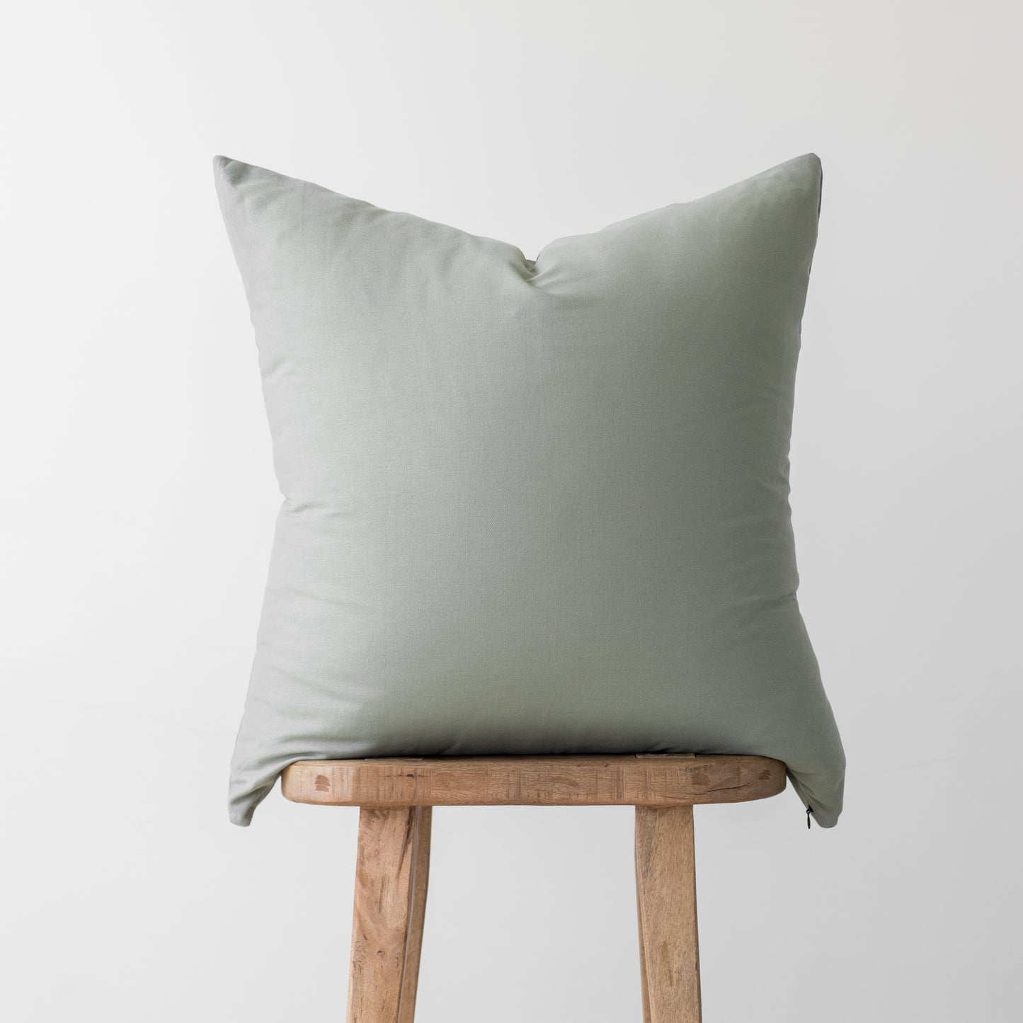 Sage green linen pillow cover with envelope closure displayed on wooden stool.
