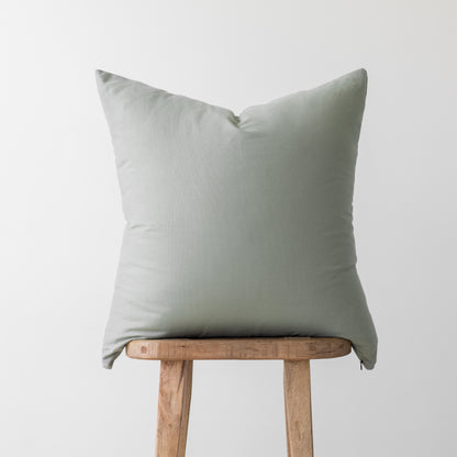 Sage green linen pillow cover with envelope closure displayed on wooden stool.