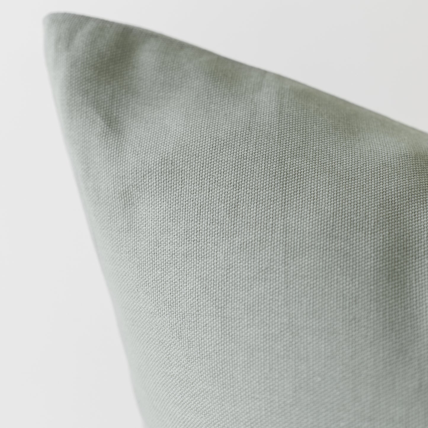 Sage green woven pillow cover with textured fabric surface shown at an angle.