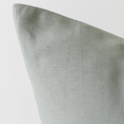 Sage green woven pillow cover with textured fabric surface shown at an angle.