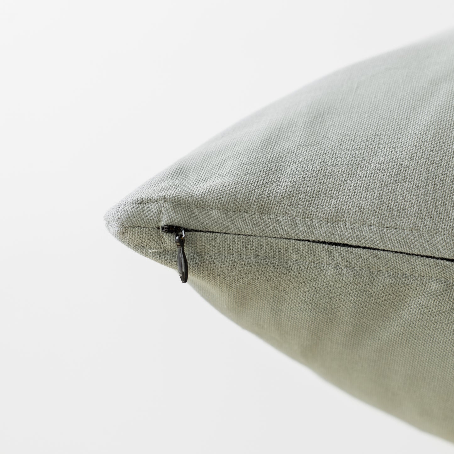 Sage-colored pillow with textured fabric and black zipper closure.