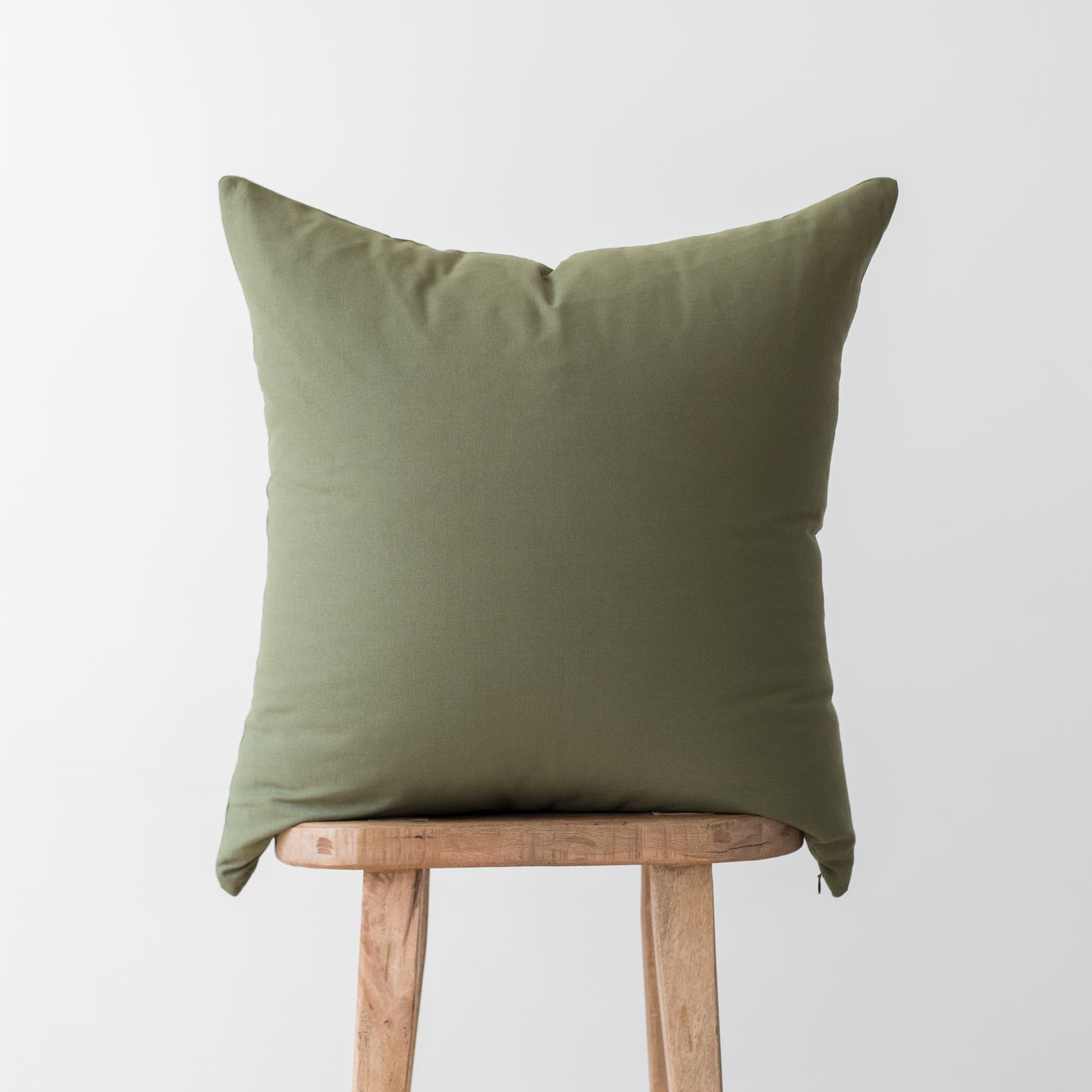 Olive green square pillow cover displayed on wooden stool.