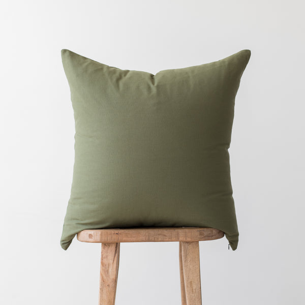 Olive green square pillow cover displayed on wooden stool.