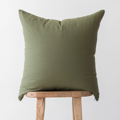 Olive green throw pillow with solid linen texture displayed on wooden stool.
