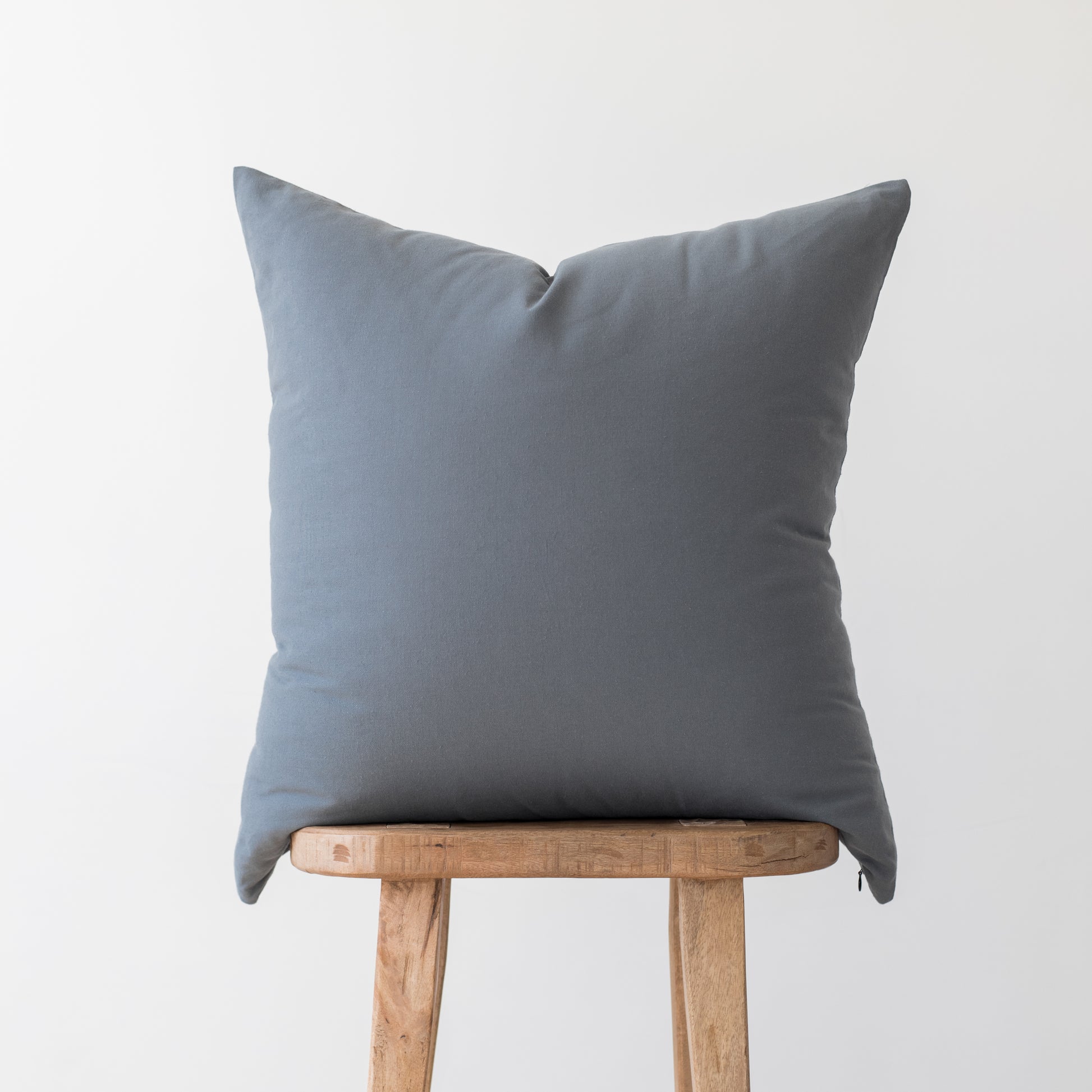 Gray linen throw pillow displayed on a wooden stool against a white background.