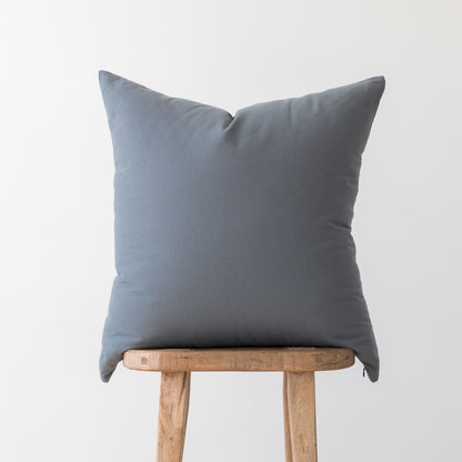 Gray linen throw pillow displayed on a wooden stool against a white background.