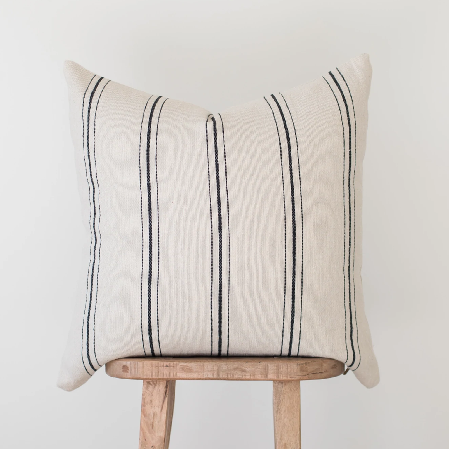 Cream linen pillow with black vertical stripe pattern displayed on wooden chair.