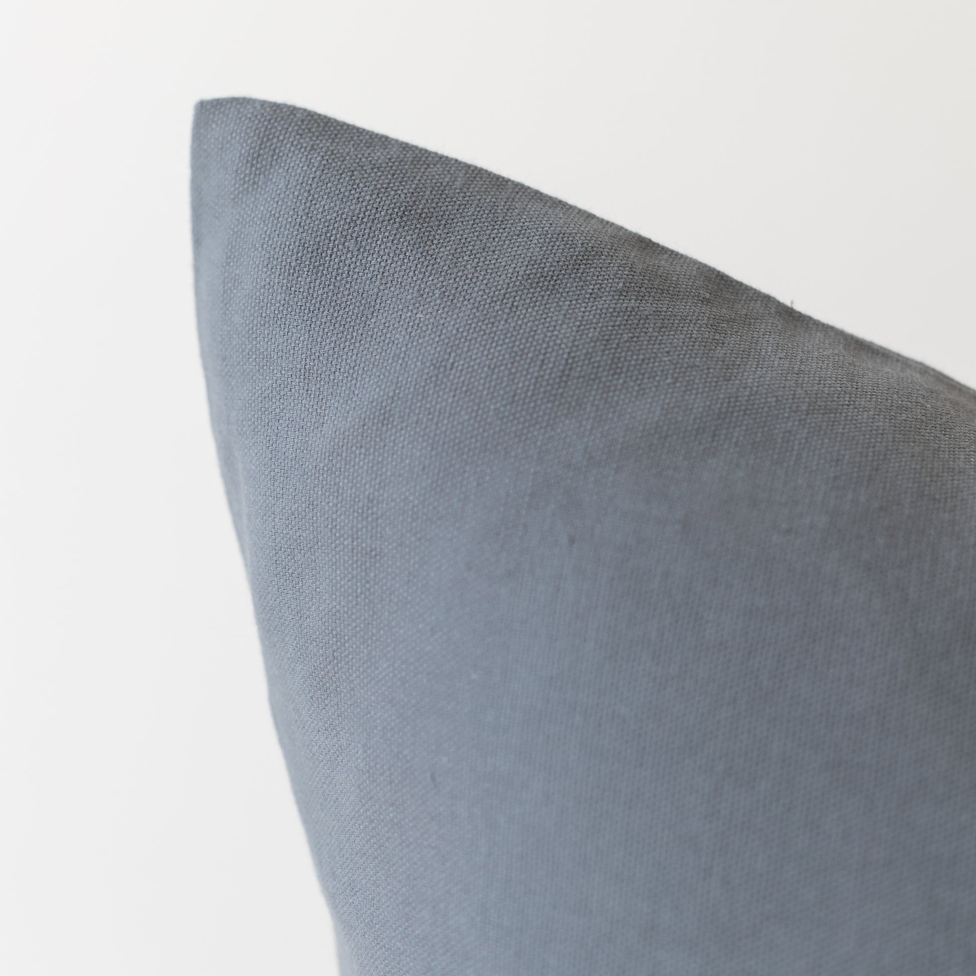 Gray woven pillow with visible corner seam and textured fabric surface.