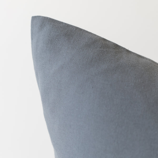Gray woven pillow with visible corner seam and textured fabric surface.