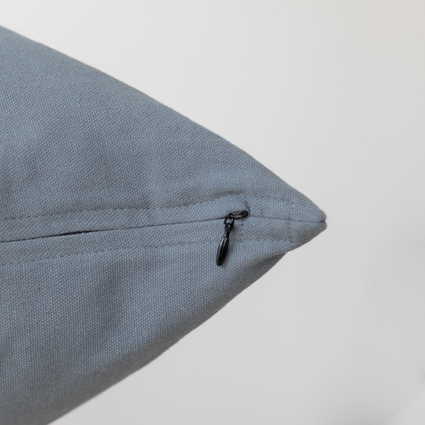 Blue-gray textured pillow with black zipper closure on seam.