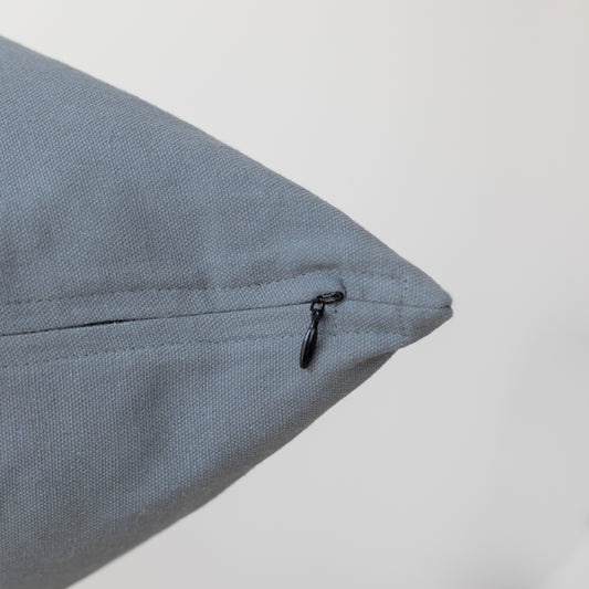 Blue-gray textured pillow with black zipper closure on seam.