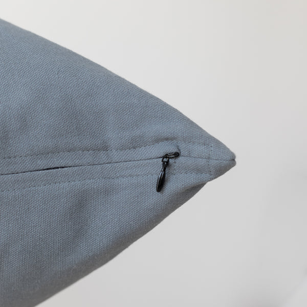 Blue-gray textured pillow with black zipper closure on seam.