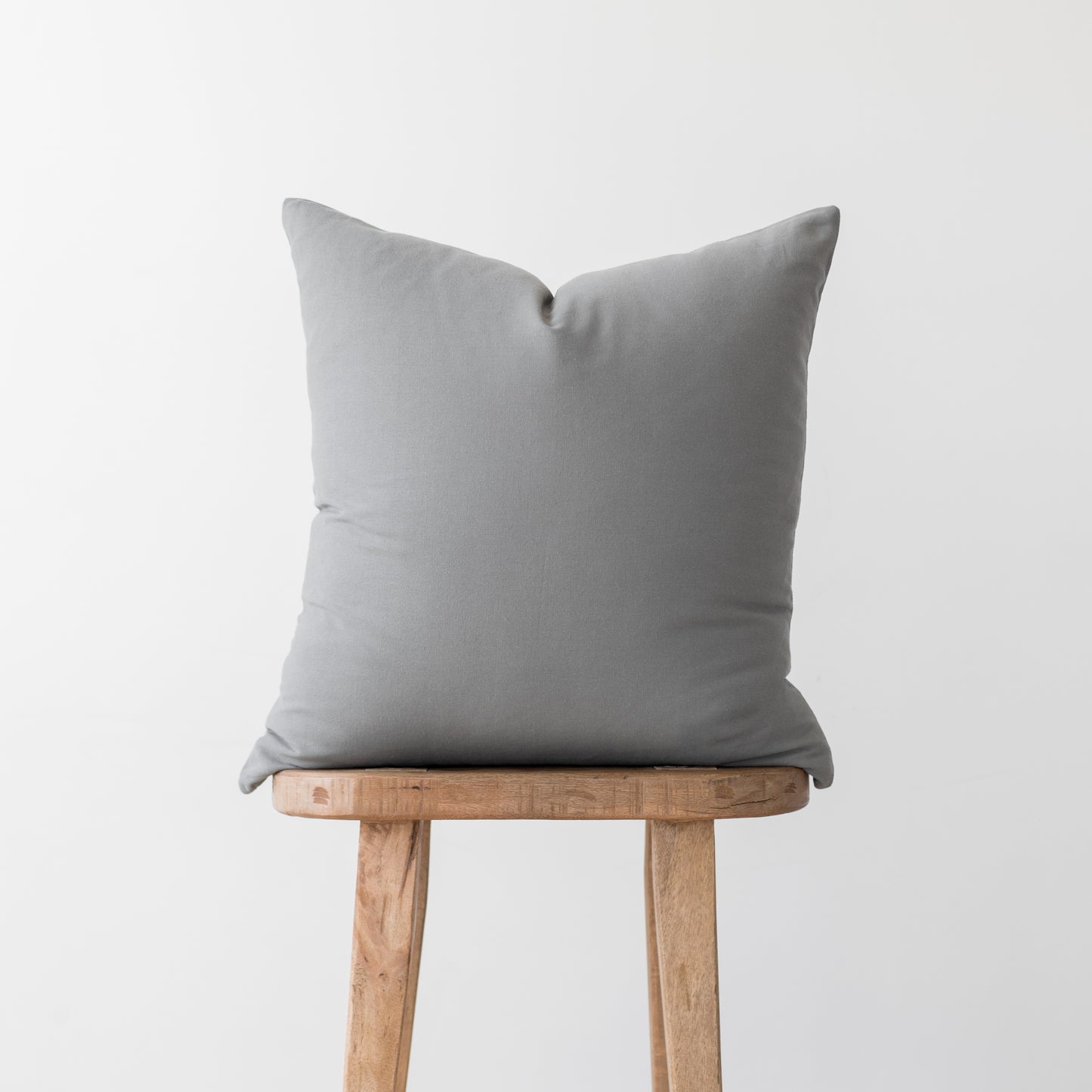Gray linen pillow cover with envelope closure displayed on wooden stool.