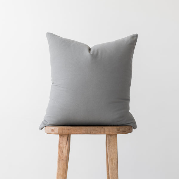 Gray linen pillow cover with envelope closure displayed on wooden stool.