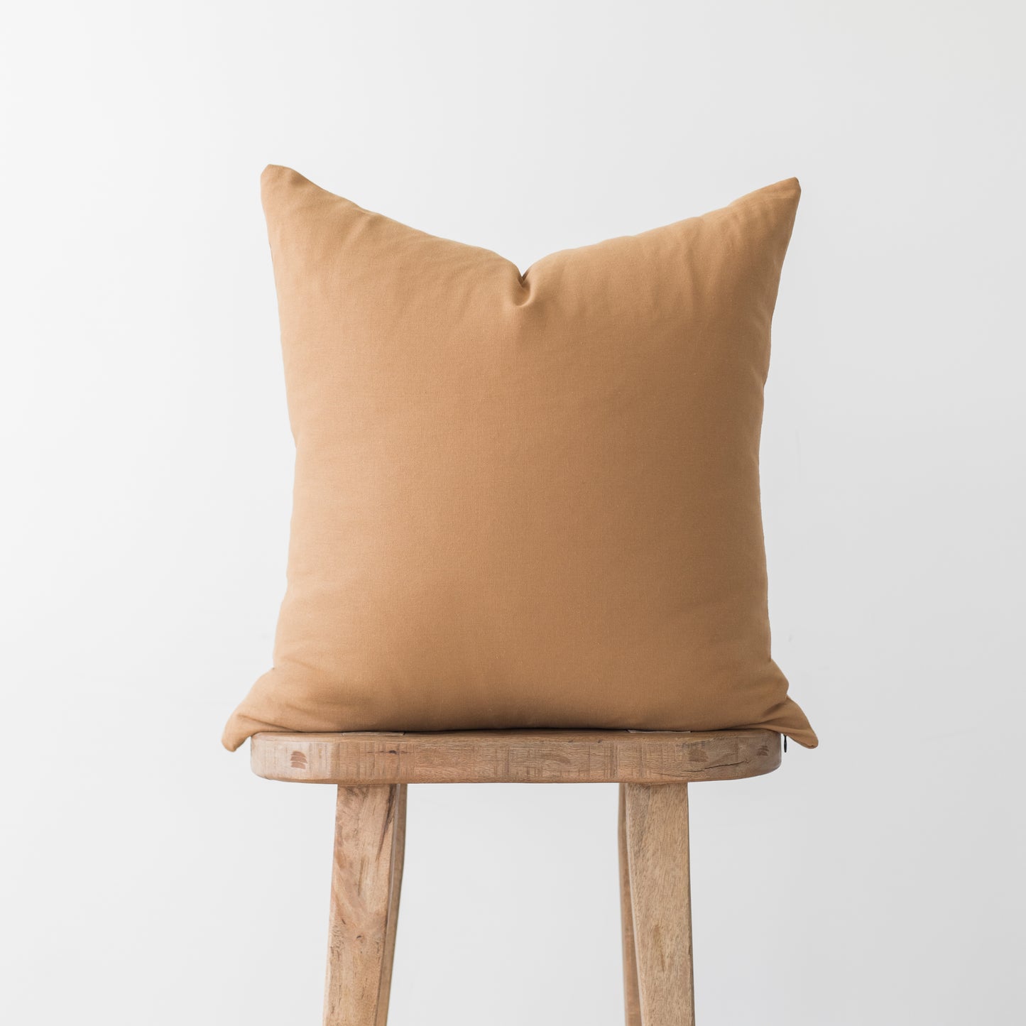 Terracotta-colored pillow with solid fabric displayed on wooden stool.