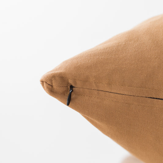 Terracotta-colored woven pillow with zipper closure and textured fabric surface.