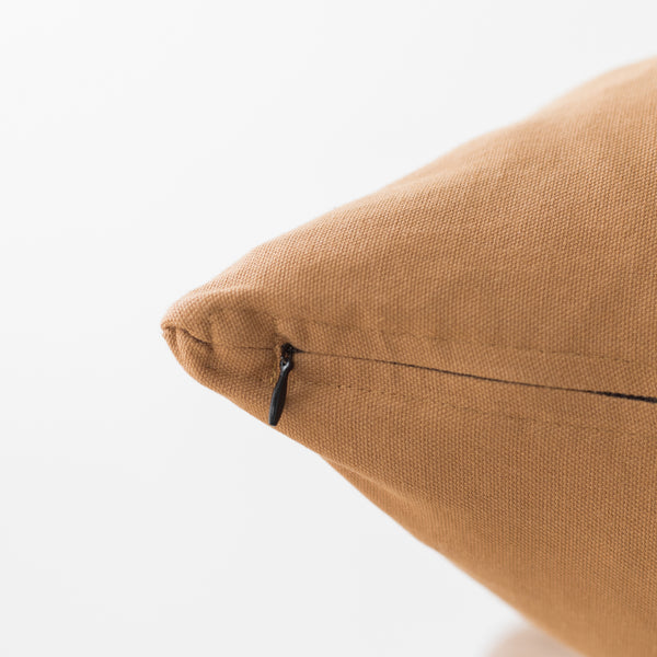 Terracotta-colored woven pillow with zipper closure and textured fabric surface.