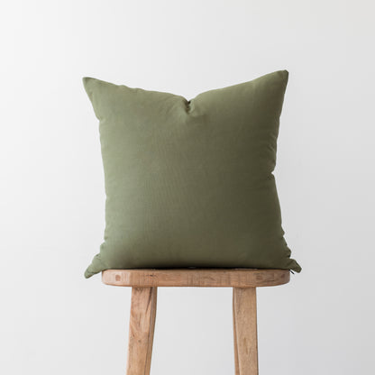 Olive-colored square throw pillow with envelope closure displayed on wooden stool.