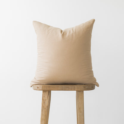 Cream-colored square pillow with knife edge seam displayed on wooden stool.