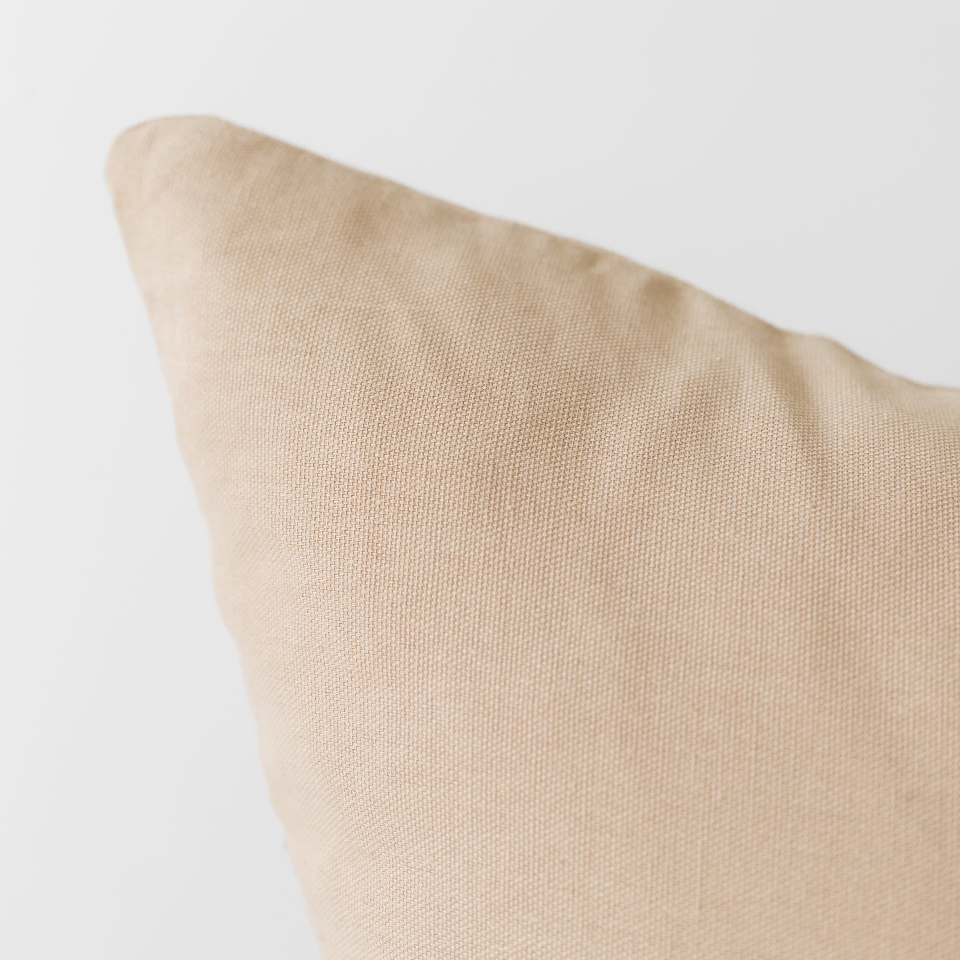Cream-colored woven pillow cover with visible texture and piped edge detail.