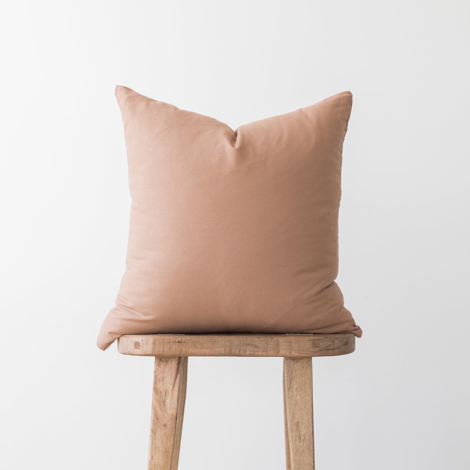 Dusty rose square pillow cover displayed on wooden stool against neutral background.