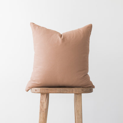 Dusty rose square pillow cover displayed on wooden stool against neutral background.