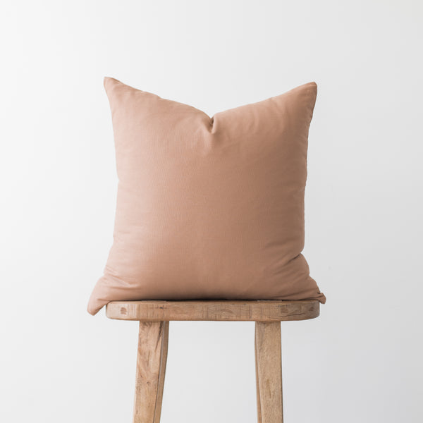 Dusty rose square pillow cover displayed on wooden stool against neutral background.