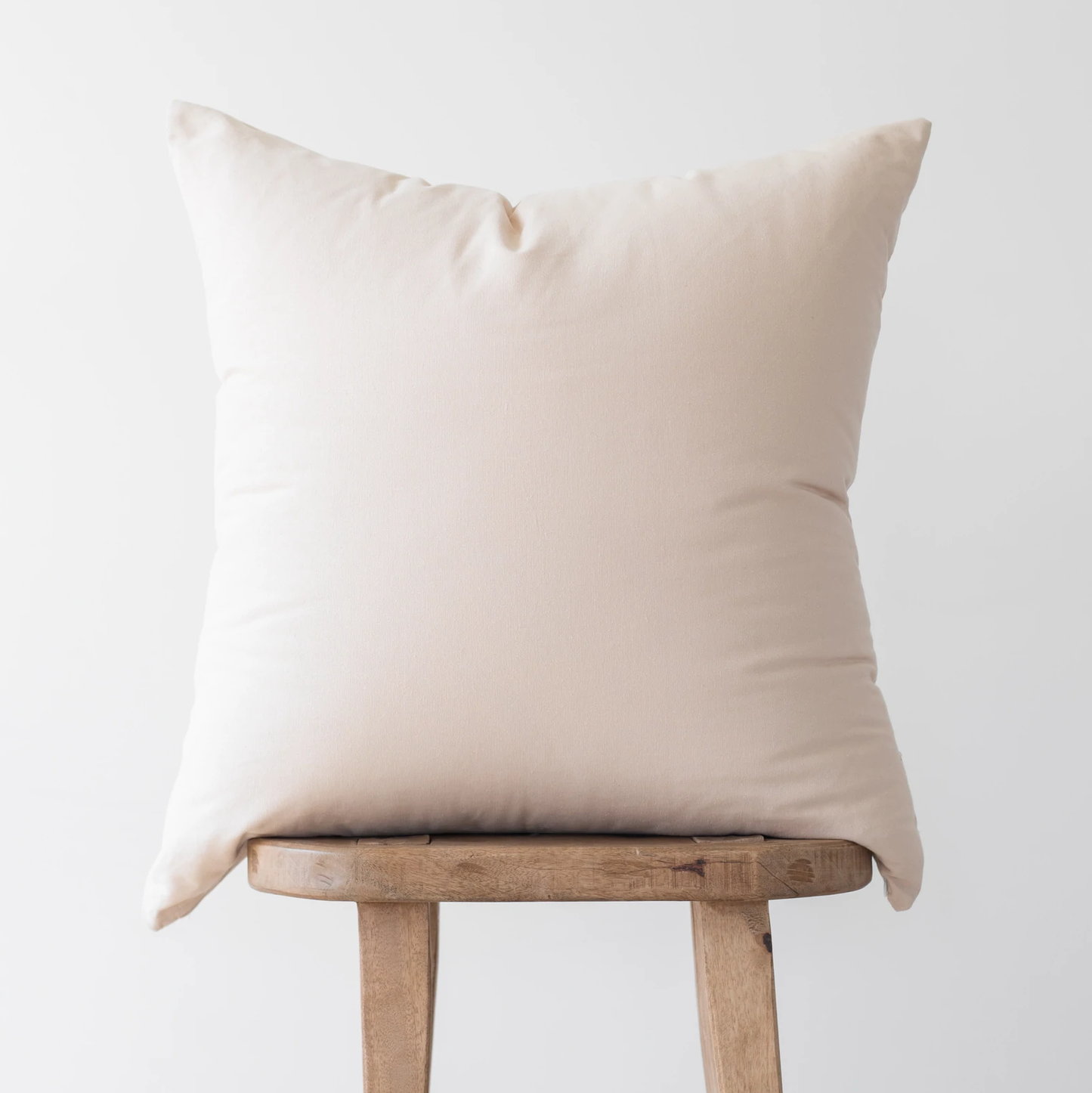 Cream-colored solid pillow cover with envelope closure, displayed on a wooden stool.