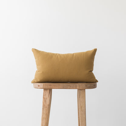 Gold rectangular pillow with solid fabric resting on wooden stool.