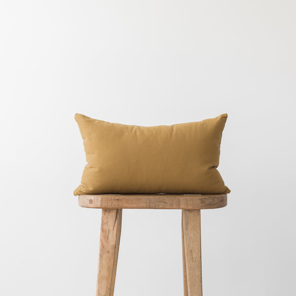 Gold rectangular pillow with solid fabric resting on wooden stool.