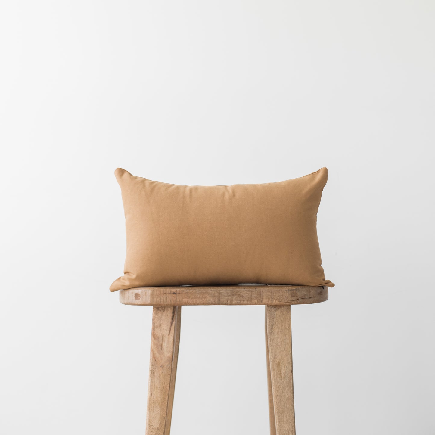 Terracotta rectangular pillow on wooden stool with neutral background.