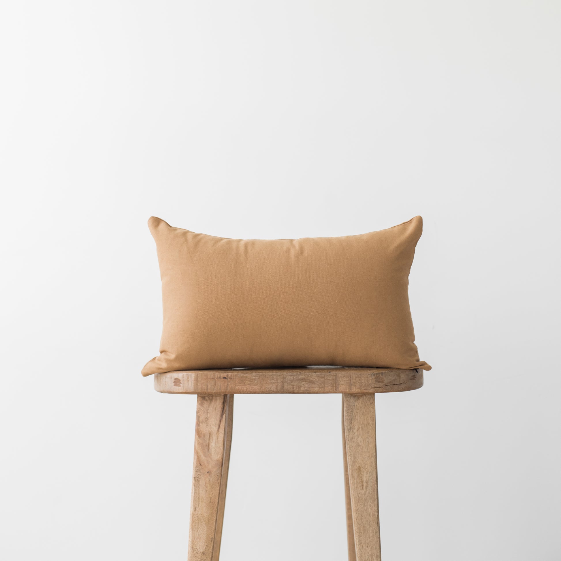 Terracotta rectangular pillow on wooden stool with neutral background.