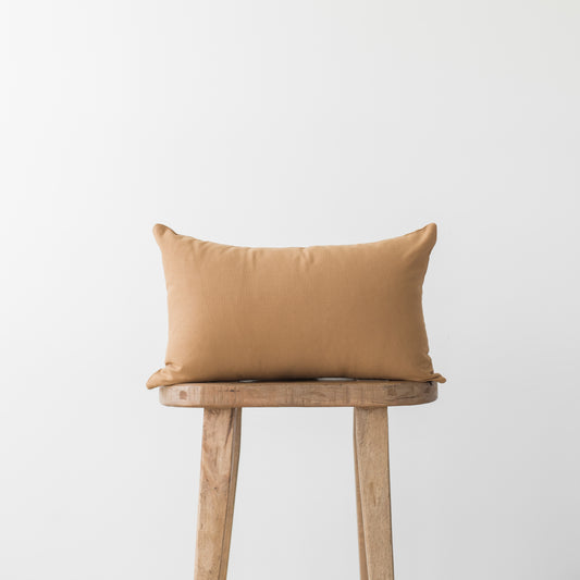 Terracotta rectangular pillow on wooden stool with neutral background.
