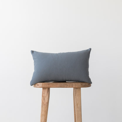 Blue-gray lumbar pillow displayed on a wooden stool against a white background.